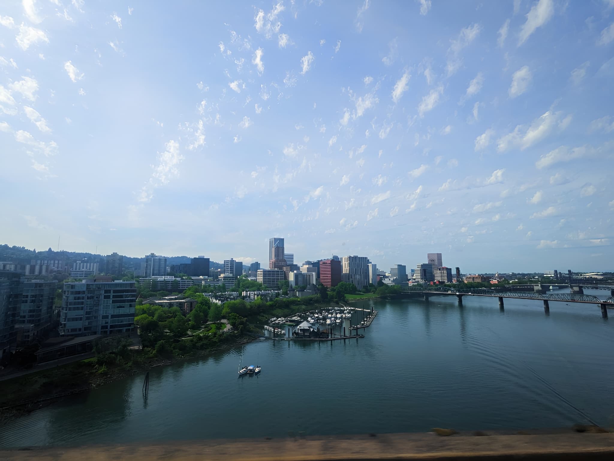 Portland skyline overlooking the Willamette River with a marina and bridge under wispy clouds.