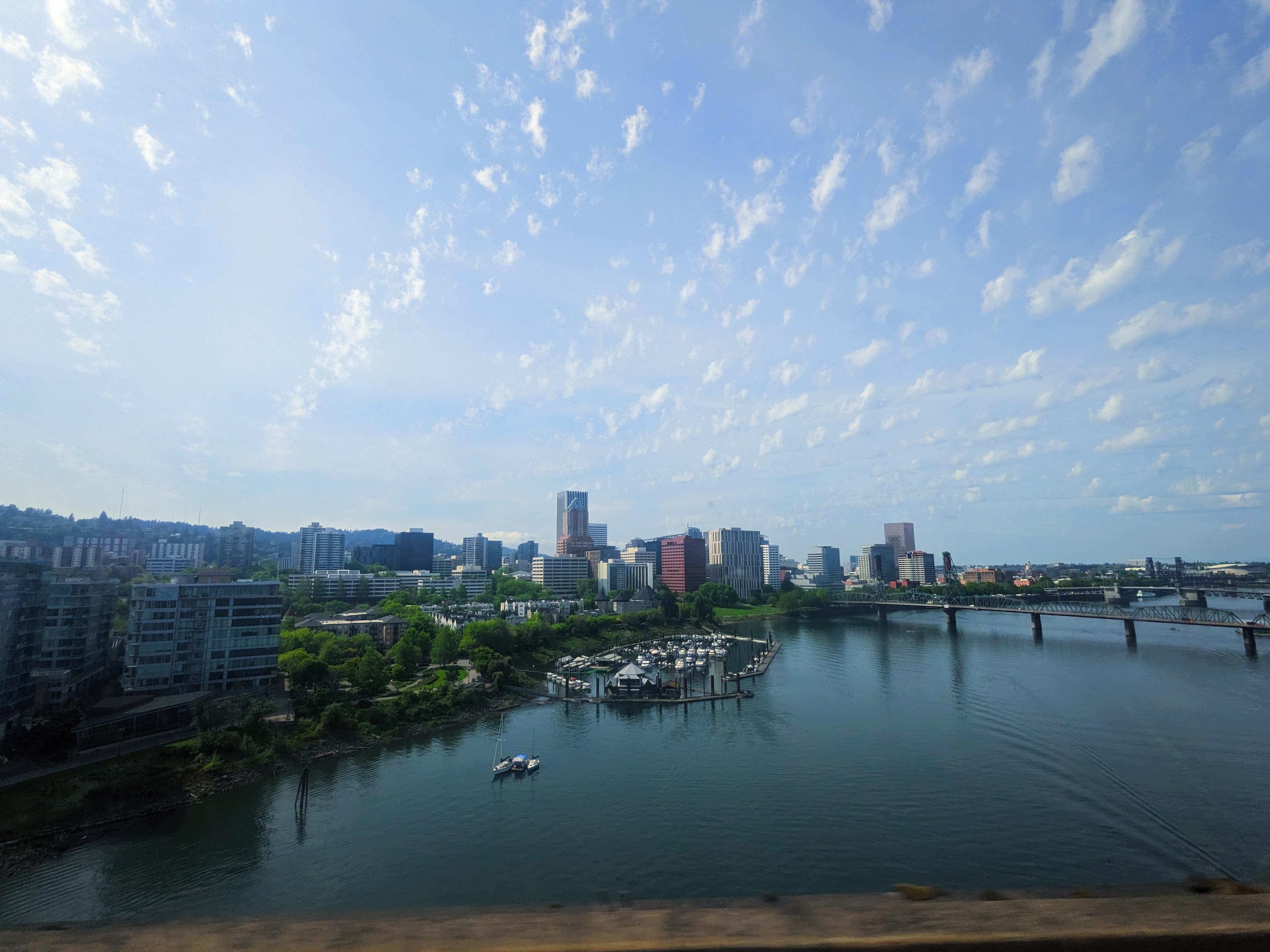 Portland skyline and Willamette River with a marina and bridges under a wispy blue sky.